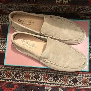 Beige mockaloafers från Loro Piana - Snygga beige loafers från Loro Piana i mjuk mocka. Perfekta för en stilren och avslappnad look. Skorna har en klassisk design med en vit sula som ger en modern touch. Perfekta för sommarens alla tillfällen.
