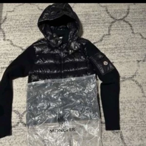 Svart jacka från Moncler - Snygg svart jacka från Moncler med quiltad design och huva. Jackan har långa ärmar och en logotyp på ärmen. Perfekt för kyligare väder.