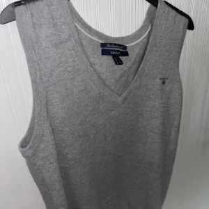 Grå stickad väst från GANT - Snygg grå stickad väst från GANT med v-ringad design. Perfekt för lager-på-lager stil. Diskret logga på bröstet ger en stilren touch. Sörjer att den ej kommer till användning. Storlek L men perfekt för mig som är S/XS. Nypris 1000-1100kr! Ofta slut på Gants hemsida! Första o sista bilden mina.