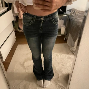 Blå bootcut jeans med broderade bakfickor - Snygga blå bootcut jeans med broderade detaljer på bakfickorna. De har en klassisk femficksdesign och en knappgylf. Perfekta för en avslappnad stil.