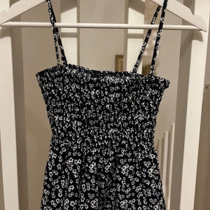 Blommig volang tröja från Gina Tricot - Söt blommig volang tröja från Gina Tricot i svart och vit. Tröjan har smala axelband och en elastisk överdel för en bekväm passform. Perfekt för varma dagar och somriga äventyr.