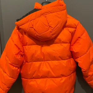 Orange pufferjacka från Carhartt - Säljer en cool orange pufferjacka från Carhartt med huva och dragkedja. Jackan har en praktisk ficka framtill och är perfekt för kyliga dagar. Den är i en iögonfallande färg som verkligen sticker ut. Perfekt för dig som vill ha både stil och funktion! Vill lägga till att den har används 2 gånger då jag köpte för stor storlek! Hör av er vid intresse😊