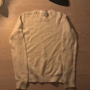 Vit stickad tröja från VILA - Säljer en stilren beige stickad tröja från Filippa K. Tröjan har en rund halsringning och långa ärmar med ribbade muddar. Perfekt för kyligare dagar och enkel att matcha med olika outfits.