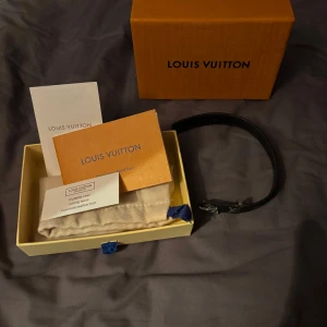 Svart armband från Louis Vuitton - Säljer ett stilrent svart armband från Louis Vuitton med klassiskt monogrammönster. Armbandet har en elegant spänne med LV-logotypen. Perfekt för att ge en lyxig touch till din outfit. Levereras med originalförpackning.