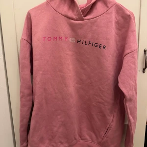 Rosa hoodie från Tommy Hilfiger - Säljer en snygg rosa hoodie från Tommy Hilfiger med logotypen tryckt på bröstet. Tröjan har långa ärmar, fickor på sidorna och en klassisk huva. Perfekt för en avslappnad stil. Pris kan diskuteras💕🤩