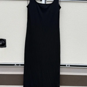 Svart ribbad klänning - Snygg svart ribbad klänning med en enkel och stilren design. Klänningen har en lös passform och är ärmlös, vilket gör den perfekt för olika tillfällen. Den är tillverkad i ett mjukt och bekvämt material som ger en skön känsla hela dagen.
