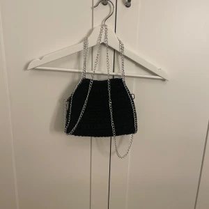 Svart stickad axelväska med kedja - Snygg svart stickad axelväska med silverfärgad kedja som axelrem. Den långa kedjan kan man ta av. Den är i jättebra skick och ingenting som har gått sönder någon gång. Jag har även en ljusrosa och en marinblå som jag kan sälja, skriv för bilder på de