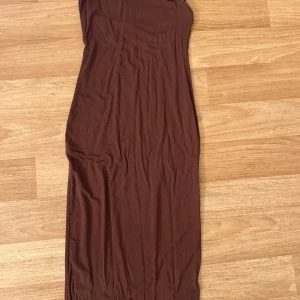 Brun axelbandslös klänning - Snygg brun axelbandslös klänning med en tight passform. Perfekt för en stilren look. Klänningen har en enkel design som gör den lätt att matcha med olika accessoarer.
