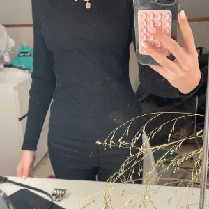 Svart ribbad tröja med knappar - Säljer en stilren svart ribbad tröja med dekorativa knappar på axeln. Tröjan har långa ärmar och en bekväm passform. Perfekt för en elegant look.