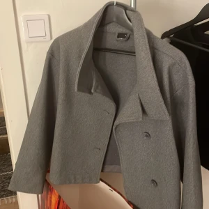 Grå kappa från Gina tricot  - Snygg grå kappa med en stilren design. Den har en klassisk krage och knappar framtill. Perfekt för kyligare dagar och ger en elegant touch till din outfit.