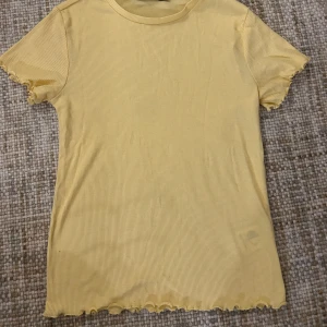 Gul ribbad t-shirt från Lager157 - Säljer en söt gul ribbad t-shirt från Lager157! Den har korta ärmar och en fin vågig kant vid ärmslut och nederkant. Jätte fin till vår/sommarn 💛