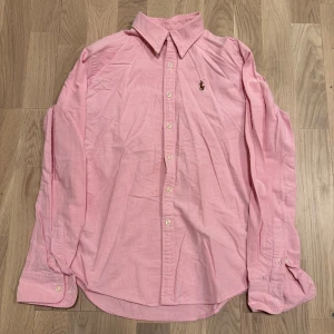 Rosa skjorta från Ralph Lauren - Snygg rosa skjorta från Ralph Lauren i slim fit. Skjortan har långa ärmar och knappar framtill. Perfekt för en stilren look med en liten broderad detalj på bröstet. Pris kan diskuteras.