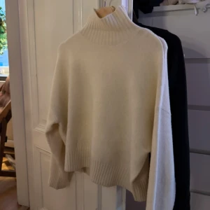 Benvit Turtle neck stickad tröja - Säljer en mysig benvit stickad polotröja med ribbade detaljer vid kragen, ärmslut och nederkant. Perfekt för kyliga dagar och ger en stilren look. Tröjan har långa ärmar och en bekväm passform. Köptes för 699kr och är i super bra skick, inga skador eller fläckar. Vid snabb affär säljer jag den för 150kr