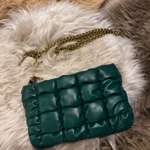 Grön axelväska med kedja - Bredd: 22cm, höjd: 14cm. Snygg grön quiltad axelväska med en guldfärgad kedja som axelrem. Väskan har en dragkedja upptill och en rymlig insida med flera småfack. Väskans axelrem är trasig - se sista bild, därav det låga priset. När du köper får du välja om du ha med remmen (om du själv vill laga den) eller om du inte vill ha remmen med! Kostar inget extra med andra ord. Köpt på Primark i London, själva väskan är i bra skick. 