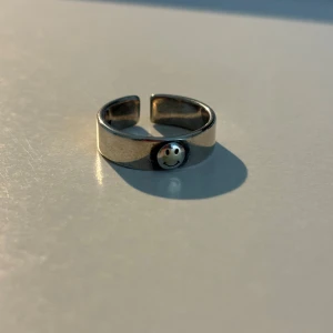 Silverfärgad ring med smiley - Trendig silverfärgad ring med en glad smiley-detalj framtill. Ringen är justerbar och passar de flesta storlekar. Perfekt för att ge en lekfull touch till din stil.