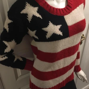 Stickad tröja med stjärnor och ränder från Gina Tricot - Säljer en stickad tröja från Gina Tricot med Amerikanska flagga design. Tröjan har långa ärmar och en rund halsringning. Perfekt för en färgglad och unik stil!