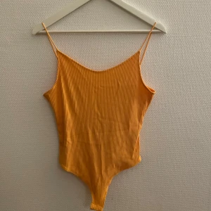Orange/gul ribbad bodysuit - Säljer en snygg orange/gul ribbad bodysuit med smala axelband. Den har en djup rygg och är perfekt för sommardagar. Passar bra till både jeans och kjol.