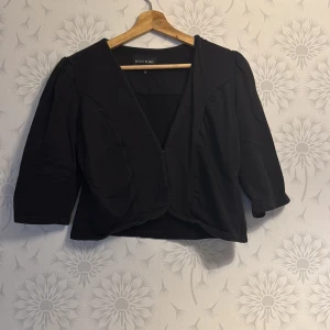 Svart kavaj från Bodyflirt - Snygg svart kavaj från Bodyflirt med trekvartsärmar och en elegant design. Kavajen har en diskret knäppning framtill och är perfekt för en stilren look. Passar bra till både vardag och festliga tillfällen.