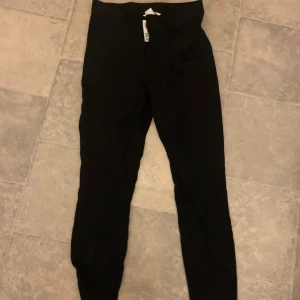 Svarta leggings - Snygga svarta leggings med dragkedja och knapp, perfekta för vardagsbruk. De har en elastisk midja för extra komfort och är tillverkade i ett mjukt material som ger en skön passform. Oanvändna 