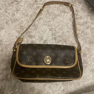 Brun axelväska med detaljer  - Snygg brun axelväska  och gulddetaljer  och elegant spänne framtill. Perfekt för att ge din outfit en lyxig touch. Bra skick släppt lite på remmen man kan trycka till med lite lim om man tycker det stör 