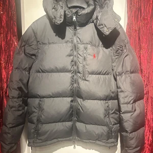 Svart Polo Ralph Lauren jacka - Snygg svart dunjacka från Polo Ralph Lauren med dragkedja och huva. Jackan har en broderad röd logotyp på bröstet och är perfekt för kalla dagar. Den har en klassisk design med långa ärmar och en bekväm passform. Priset kan diskuteras 🍾Hör av er vid minsta fundering 🍾