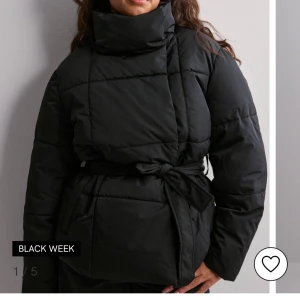 Svart quiltad pufferjacka med knytning  - Snygg svart pufferjacka med quiltad design och knytband i midjan. Jackan har en hög krage och långa ärmar, perfekt för kyliga dagar. En stilren och modern look för vintern. Slutsåld 