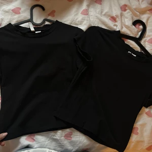 Svarta t-shirts - Två svarta t-shirts i enkel design. De har rund hals och korta ärmar, vilket gör dem till ett mångsidigt val för olika tillfällen.