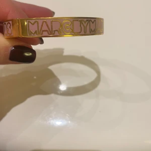 Guldarmband från Marc by Marc Jacobs - Snyggt guldarmband från Marc by Marc Jacobs med rosa detaljer. Armbandet har en stilren design med märkets namn ingraverat i rosa. 