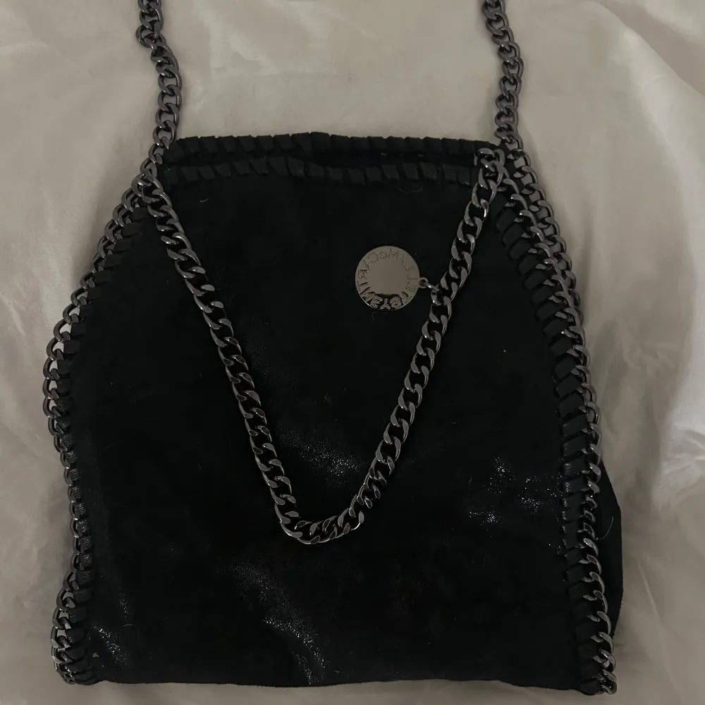 svart axelväska som liknar Stella McCartney väska! Den har en kedjedetaljer och en liten logotypbricka. Väskan har en dragkedja på baksidan för extra förvaring😻. Laukut & Käsilaukut.