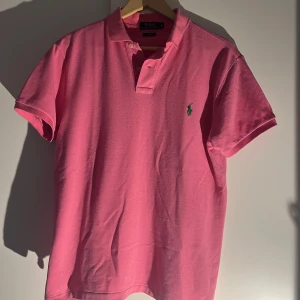 Rosa pikétröja från Ralph Lauren - Säljer en snygg rosa pikétröja från Ralph Lauren i slim fit. Tröjan har korta ärmar och en klassisk krage med knappar. Perfekt för en stilren look men lite extra. Extremt fint skick, storlek medium, säljes för endast 299 kronor🤝