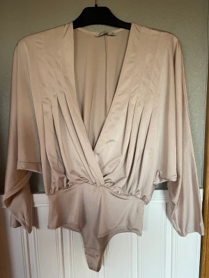 Body blankt tyg, oversize plunge body  - Body i blankt tyg, 95% polyester och 5%elastan i färgen,dusty rose Djup ringning, tre tryckknappar i grenen Ärmen går i ett med övriga tyget, avsmalnande nertill  Använd vid två tillfällen  Tvättad Från Nelly i storlek XS