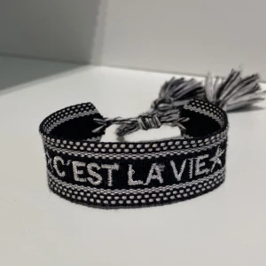 Svart/Vitt armband - Säljer denna coola armbandet med texten ”C’est la vie”. Har köpt den från någon här på plick för kanske ett halvt år sedan, och sedan dess har jag använt den max 2 ggr.  Därför är den som ny!! Priset kan diskuteras💗