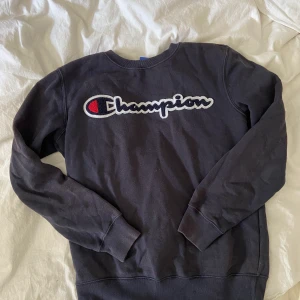 Champion collegetröja - Champion collegetröja i färg svart. Färgen är lite urtvättad men i övrigt är tröjan i nyskick - de vita prickarna är från spegeln. Storlek är i barnstorlek, jag skulle säga att det är en XS i fitten. 