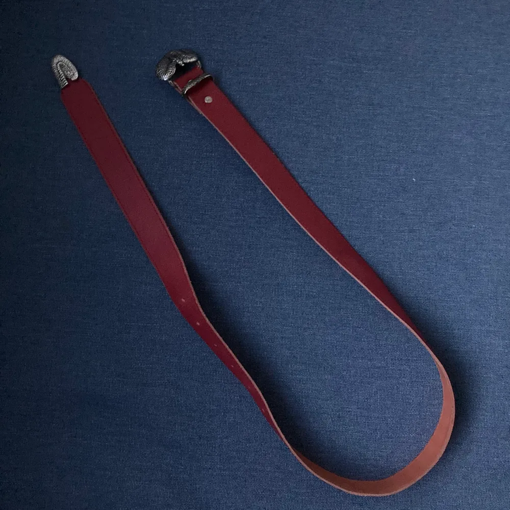 litet bälte i rött läder med buckle i metall i form av orm . Accessoarer.