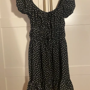 Sommarklänning  - Kort sommarklänning från ASOS, i svart med vita prickar, två knytdetaljer framtill. Går att ha som off shoulder och med söta puffiga axlar. Använd en gång. Nypris 399kr. Frakt tillkommer!!!