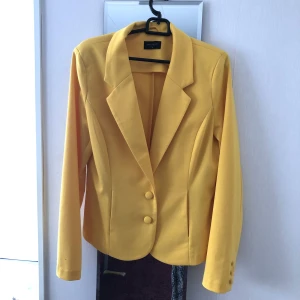 Kavaj - INTE ANVÄND. Gul kavaj från Free/Quent. Har två knappar på framsidan som fungerar och två fungerade fickor på framsidan också. Är tunn, lätt och len. Är en M men fungerar för XS och S också.  (Är mer stark gul än vad den ser ut på bild.)