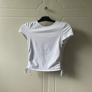 En vit t-shirt med rosetter på sidorna som man knyter. Tröjan är i bra skick.