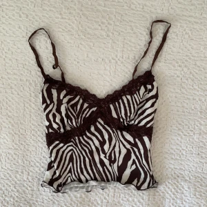 Brunt och vitt linne  - Ett brunt och vitt linne med zebramönster och spetsdetaljer. Nästan aldrig använt och i jättebra skick🤎🤎