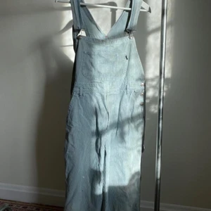 Hängselbyxor - Vit/ljusblå randiga hängselbyxor i jätte fint jeans bomulls material. Modellen är kortare i benen, tre kvarts, eller vad det kallas. Passar därför kanske bättre på en kortare person. Går till vaderna på mig som är 168. Storlek S-L beroende på längd och fit.