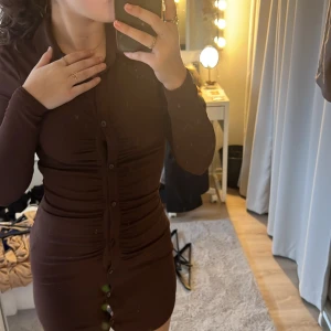 Klänning - Snygg långarmad brun klänning med knappar i mitten, aldrig använd prislapp finns kvar