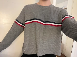 Tröja från hollister - Grå tröja från Hollister med blå/vit/röda ränder.