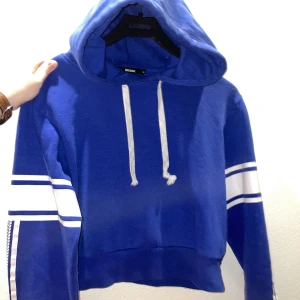 Cropped hoodie - En croppad hoodie i blått från Bik Bok med fina detaljer på ärmarna.  Endast använd 1 gång. Mjukt och behagligt material. Säljes pga den har blivit för liten för mig. Nytvättad från ett rökfritt hem, pälsdjur finns men inte på kläderna.  50kr