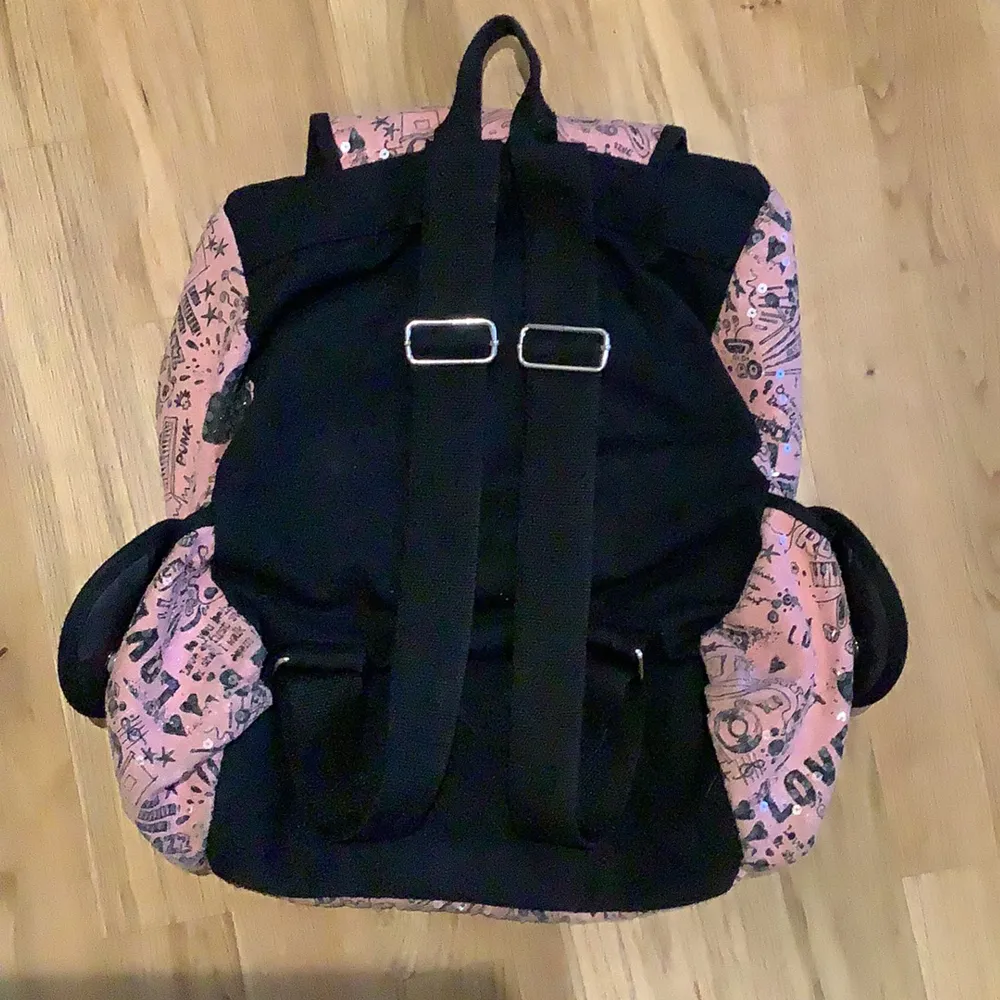 Det är en rosa väska med genomskinliga glansiga paljetter på och mönster, det finns många olika fack inuti och utanpå väskan/ryggsäcken. Den har också justeringsbara axelband.. Väskor.