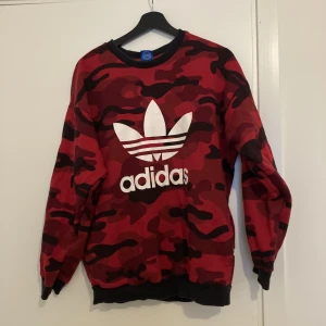 Adidas tröja med militär-mönster - Tröjan har varit regelbundet använd över längre tid. Därav är den lite nopprig (bild 2), samt att den har lätt missfärgning. Utöver detta är den i bra skick och ser fortfarande mycket fin ut! Den har ”gömda” fickor på sidane. Lite oversized fit.