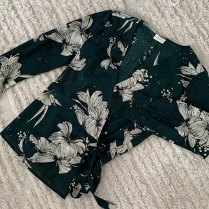 Mörkgrön omlottblus från vila  - Mörkgrön omlottblus med vita blommor från vila, storlek M. Sparsamt använd så mycket fint skick! 