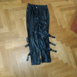 Pretty little thing byxor - Supercoola byxor med fräcka detaljer i nyskick. Storlek 42 funkar för 40 också. Utgår ifrån att det är skinnimitation. Slitsade från knä och ner där dekorspännena är 