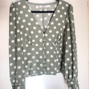 Blus från Nelly - Jättesöt prickig ljusgrön skjortblus med knappar från Nelly. V-ringning. Storlek 40. Puffiga axlar. Använd fåtal gånger. Svårt att få fram färgen på bild, skulle säga mittenbilden är mest rättvis ☺️. Extraknapp finns med.