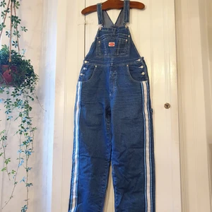 Hängselbyxor jeans/denim storlek M/L - Snickarbrallor/hängselbyxor i retro stil. Tåliga sömmar och coola detaljer längs med sidan. Nyskick och ett tåligt material.