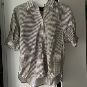 Kortärmad skjorta - Inte använd och prislappen sitter fortfarande kvar. En ajkorta med ljus nyans av beige och svarta ränder, armarna sitter lite ovanför armbågarna, skönt material för varmt väder och knappar på framsidan. Sitter super fint!