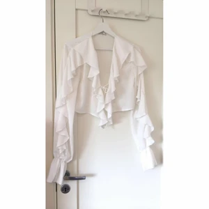 Vit blus med volanger - Somrig fin vit blus med volangdetaljer! Blusen är från Nelly i storlek s! Den är i fint skick!